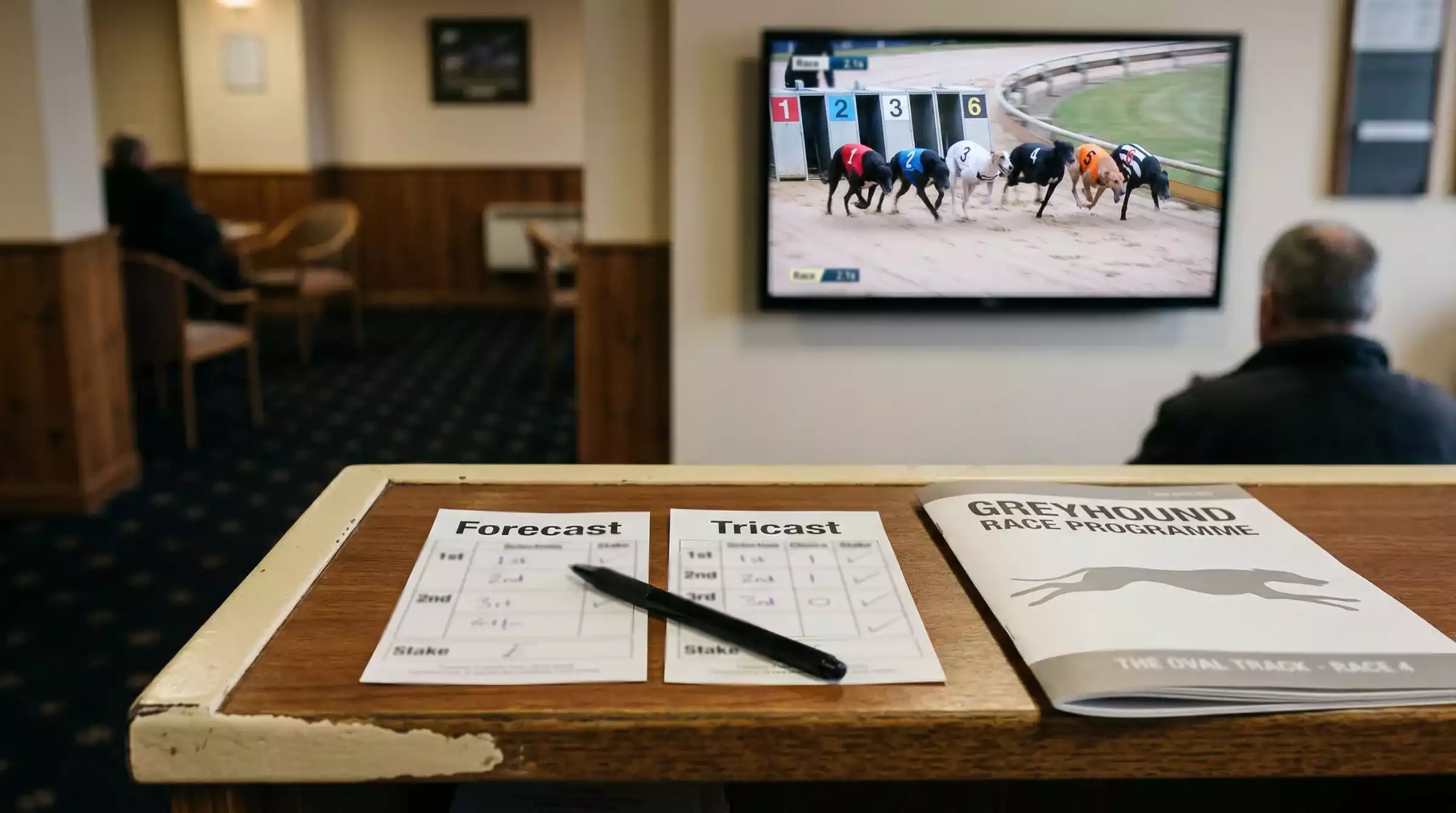 Bookmaker counter with greyhound forecast and tricast betting slips and a race programme