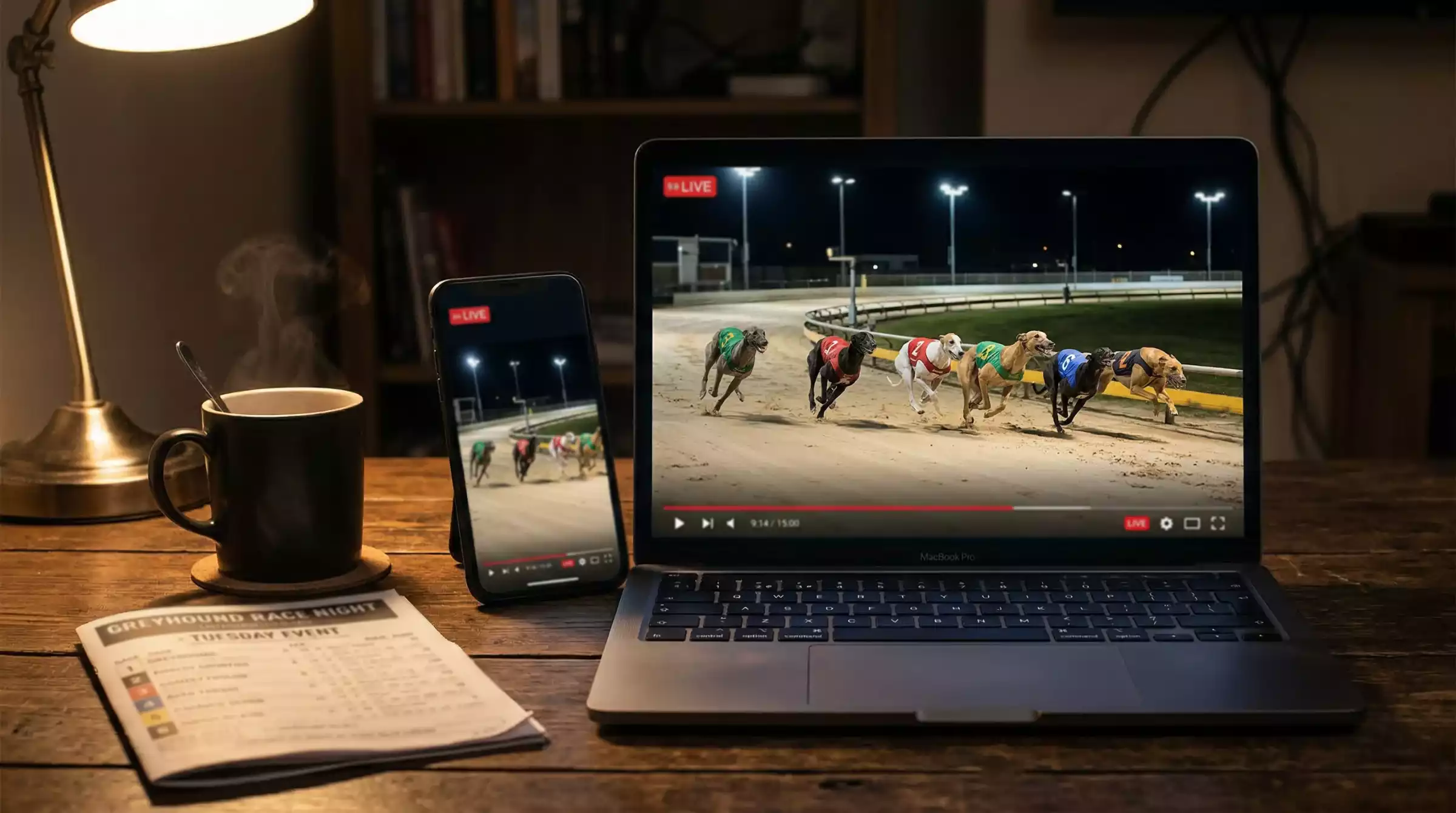 Laptop and smartphone showing a live greyhound race stream with a floodlit track on screen